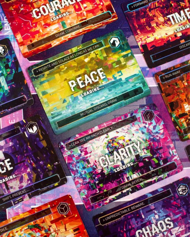 Complie: Main 2 Card game close-up, angled view of multiple colourful card faces from a deck, showing abstract pixel-art style artwork with words like COURAGE, PEACE, CLARITY, and CHAOS on the top cards.