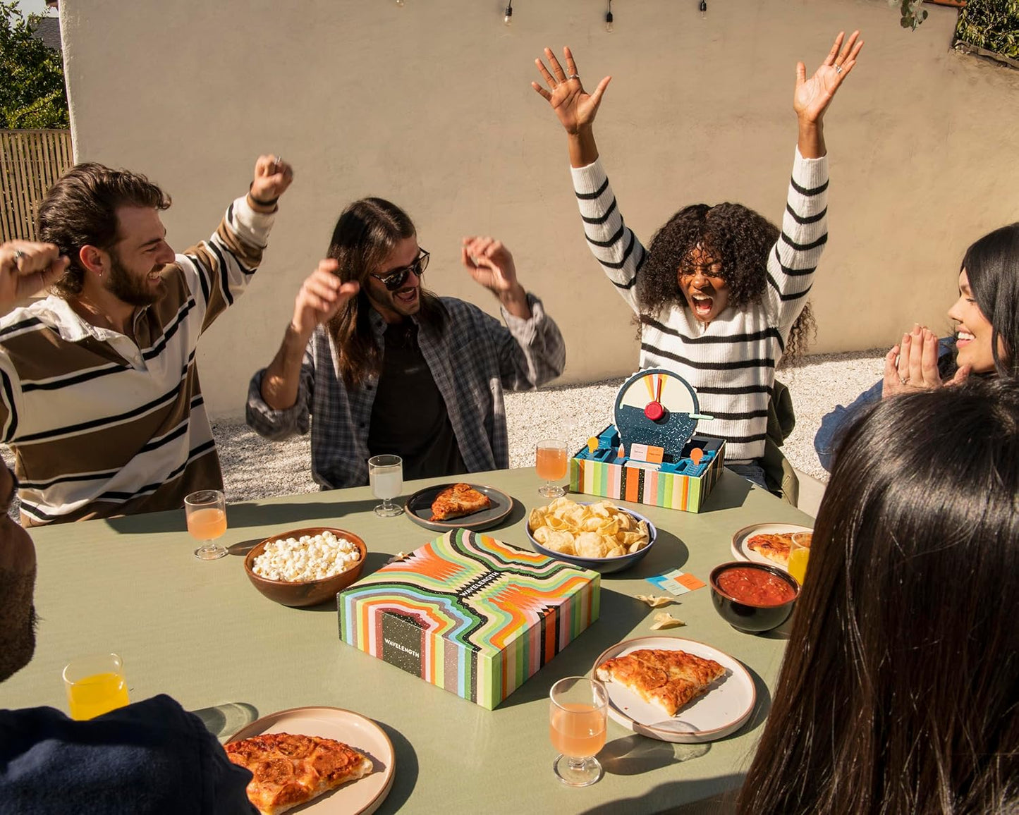 Group of people enjoying a meal playing Wavelength by CMYK with pizza and drinks.