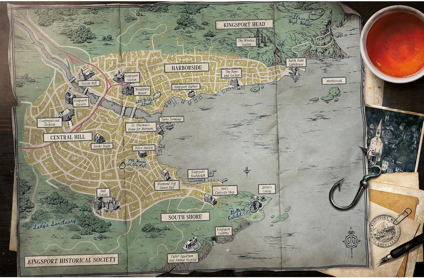 Vintage-style map of a town with labeled areas, placed on a surface with a cup and pen.