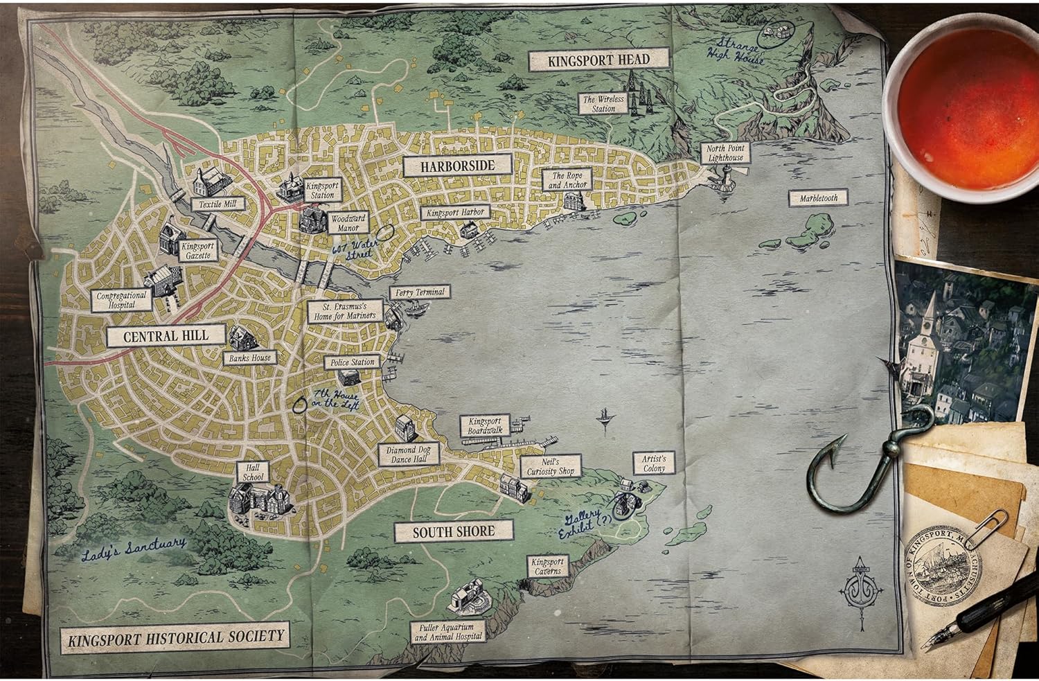Vintage-style map of a town with labeled areas, placed on a surface with a cup and pen.