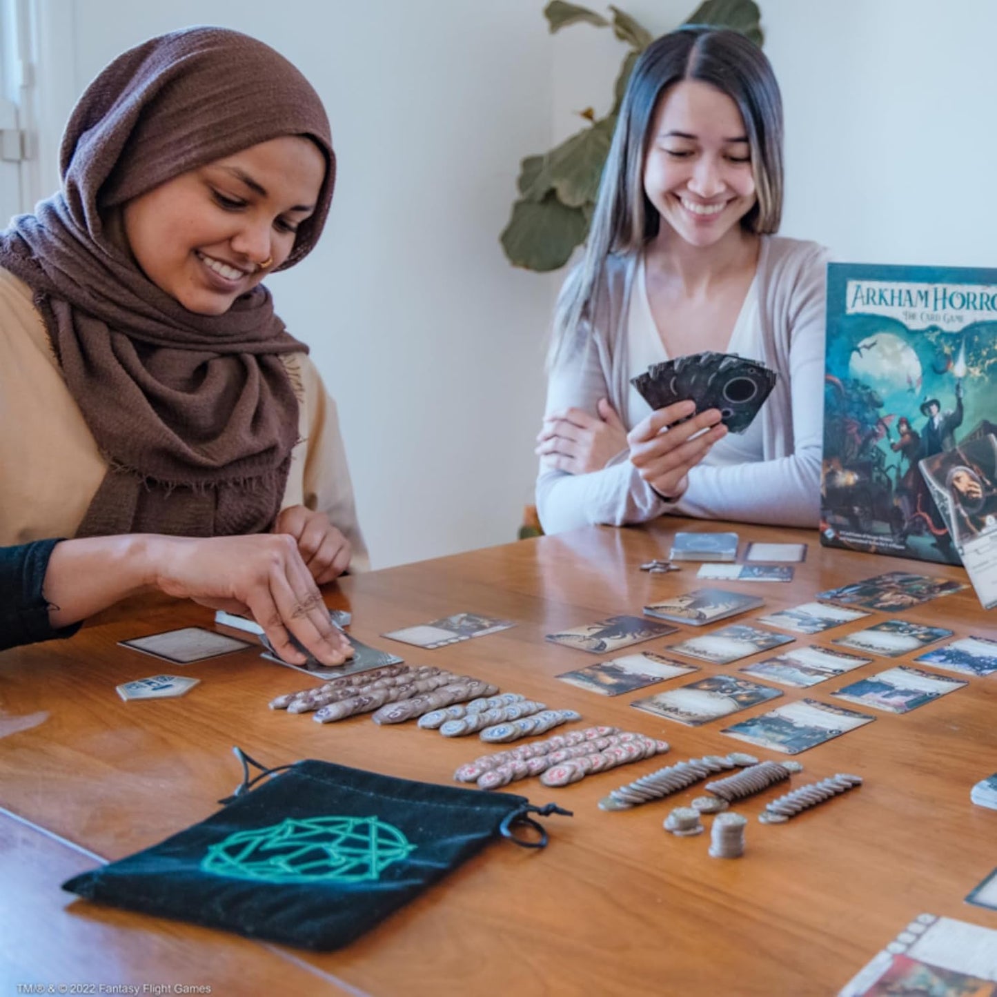 Two women playing a board game with cards and dice on a wooden table.