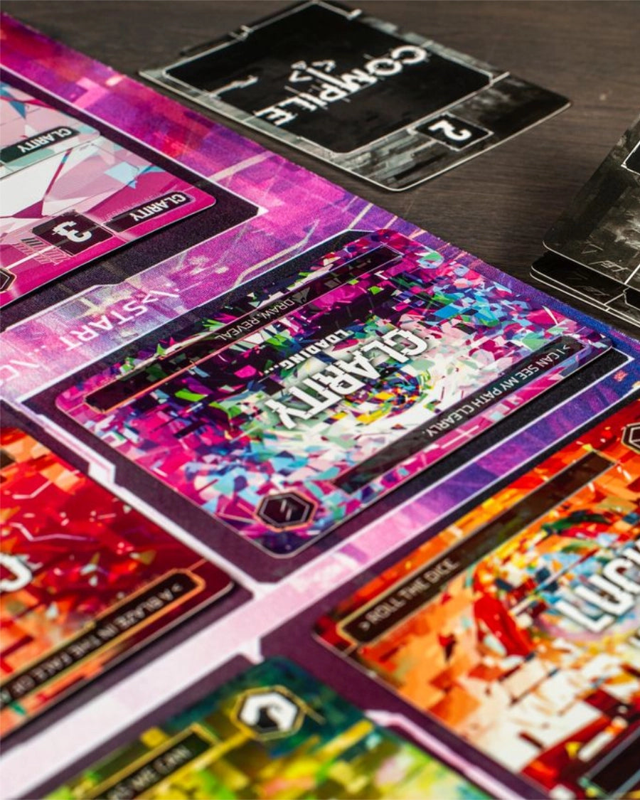 Close-up of colourful game cards for Complie: Main 2 Card game, laid out on a dark wooden surface.