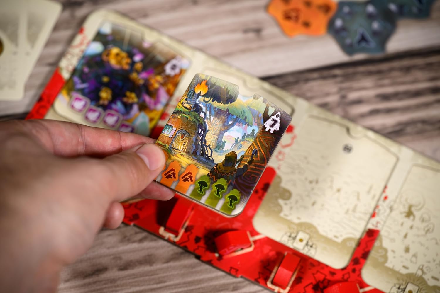Hand holding a colorful card with a Halloween-themed illustration on a wooden surface.