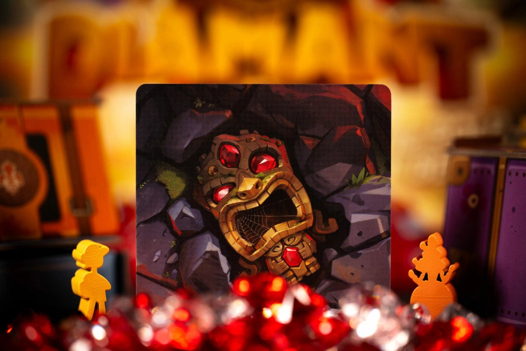 Card with a fantasy character design featuring red eyes and gold accents, surrounded by red gemstones and small figures for the board game Diamant.