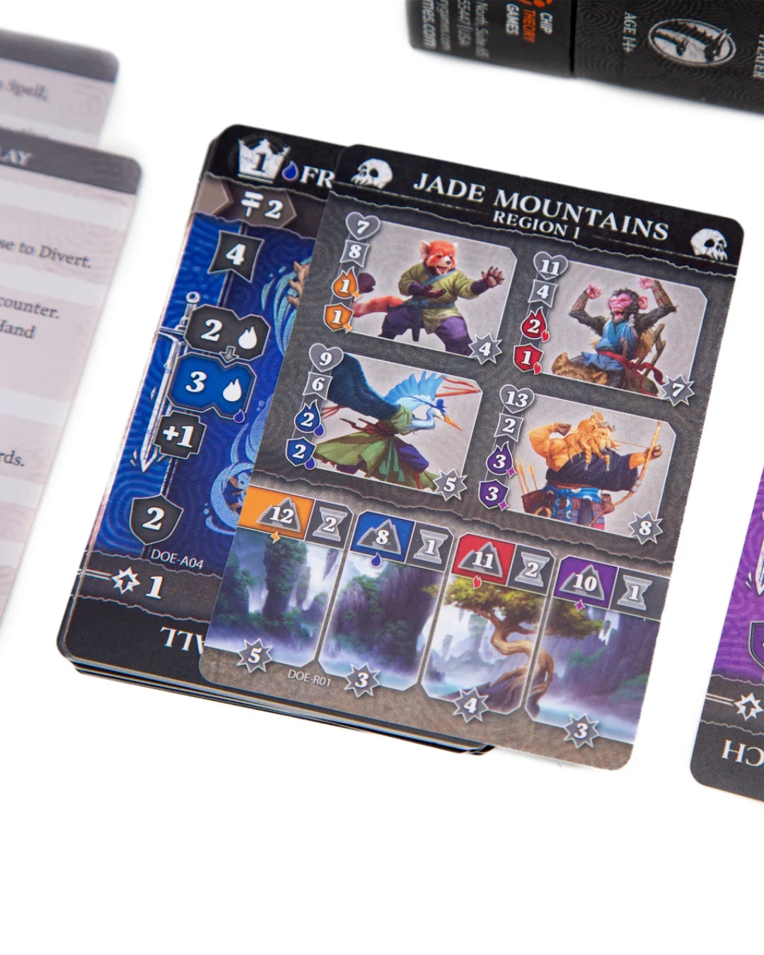 A close-up of a Dragon's of Etchinstone card deck labelled 'Jade Mountains Region 1' on a white background, with part of the box and other cards visible around it.