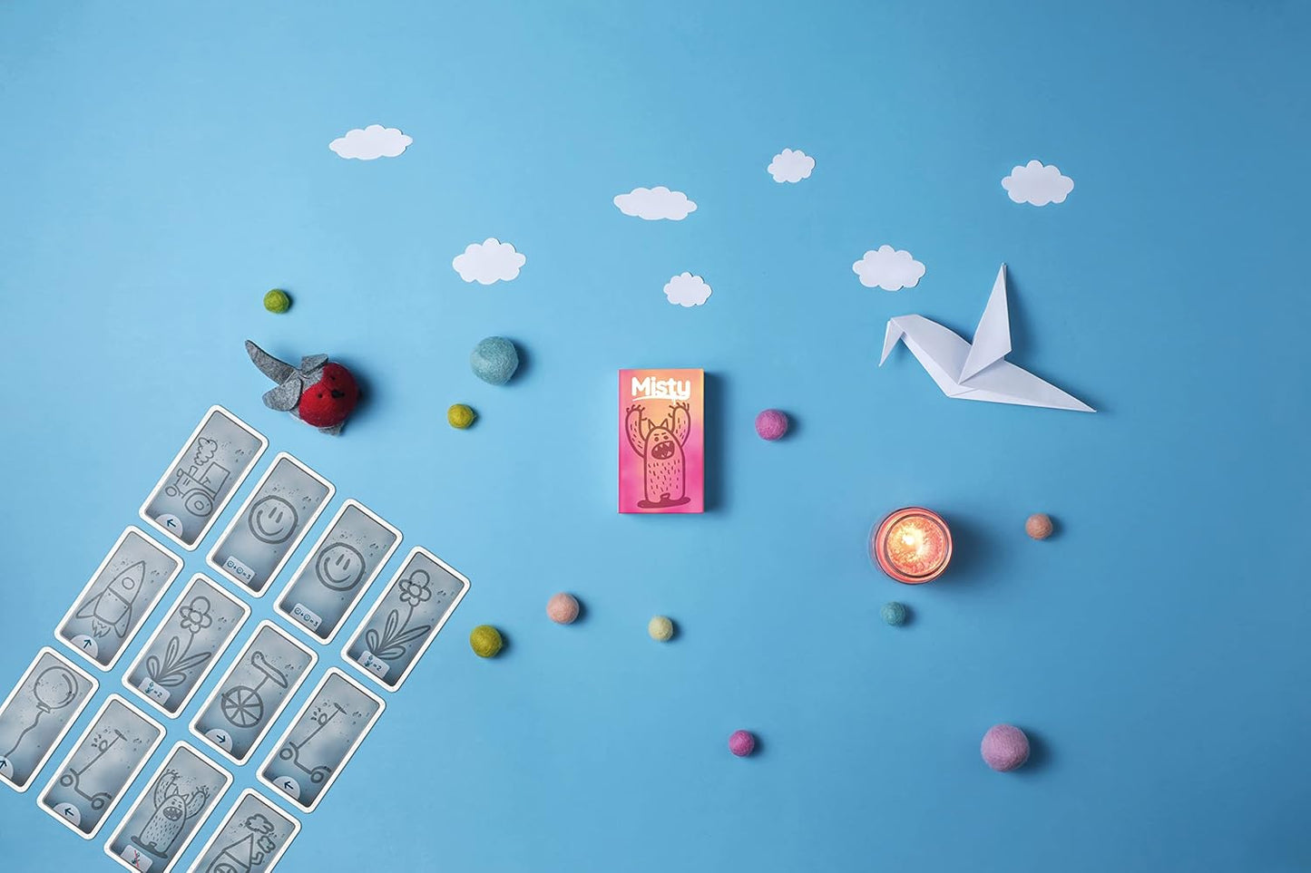 Collection of tarot cards, a small figurine, a pink card with a cat, a white paper crane, and colorful objects on a blue background.