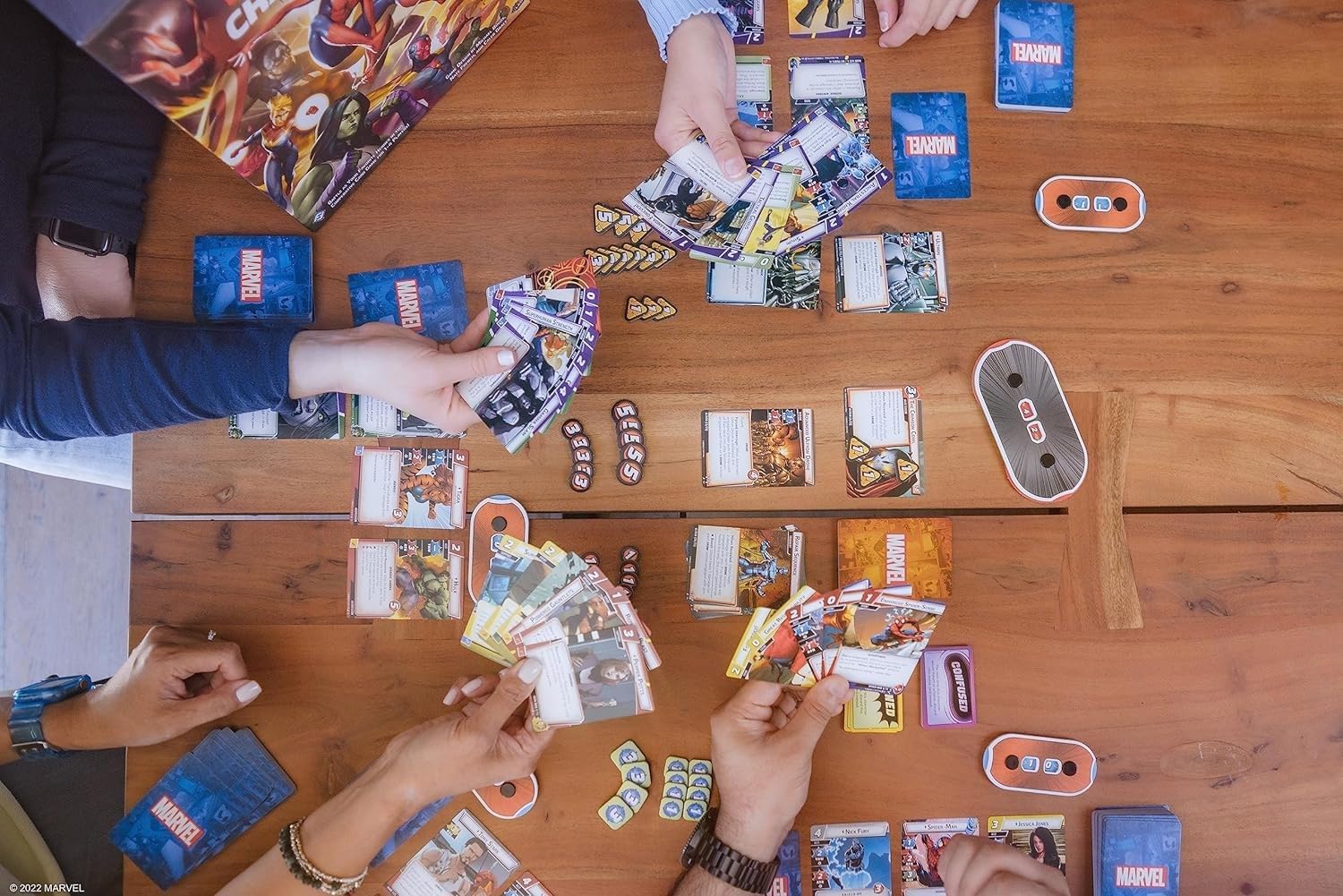 People playing Marvel Champions - The card game on a wooden table with various cards and game pieces.
