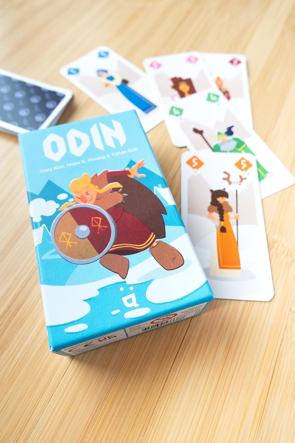 Card game box labeled 'ODIN' with cards featuring cartoon characters on a wooden surface