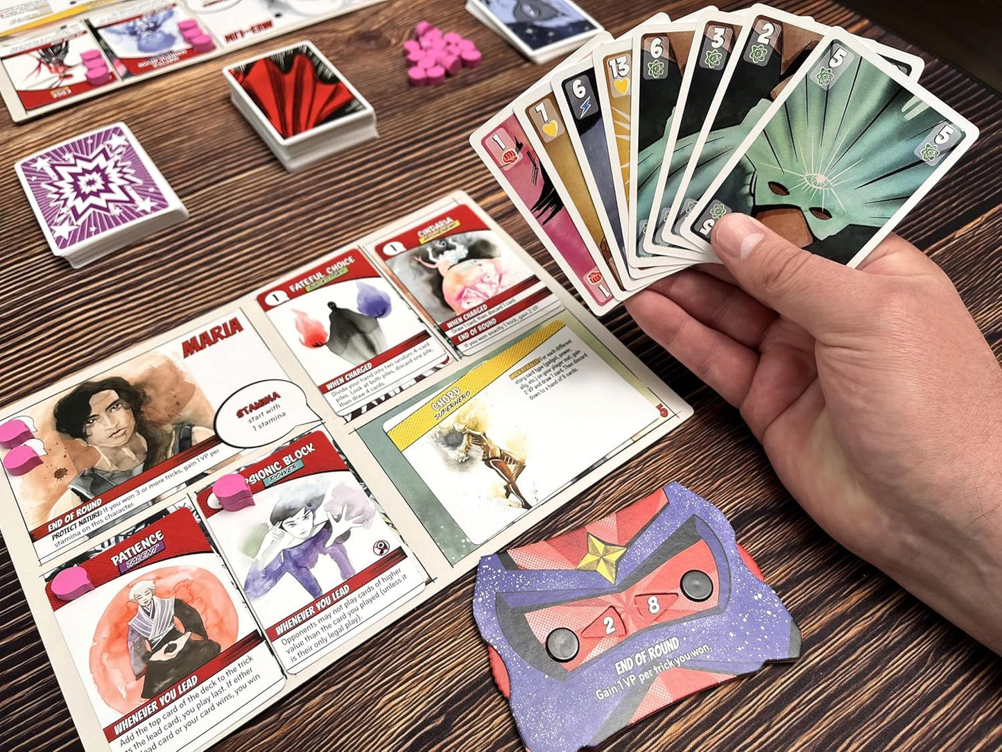 Origin Story card game on a wooden table with other cards and game pieces.