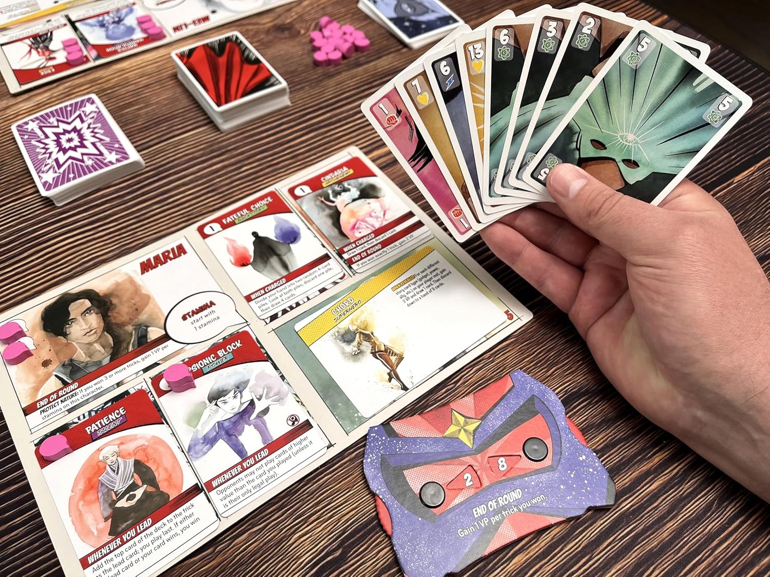 Origin Story card game on a wooden table with other cards and game pieces.