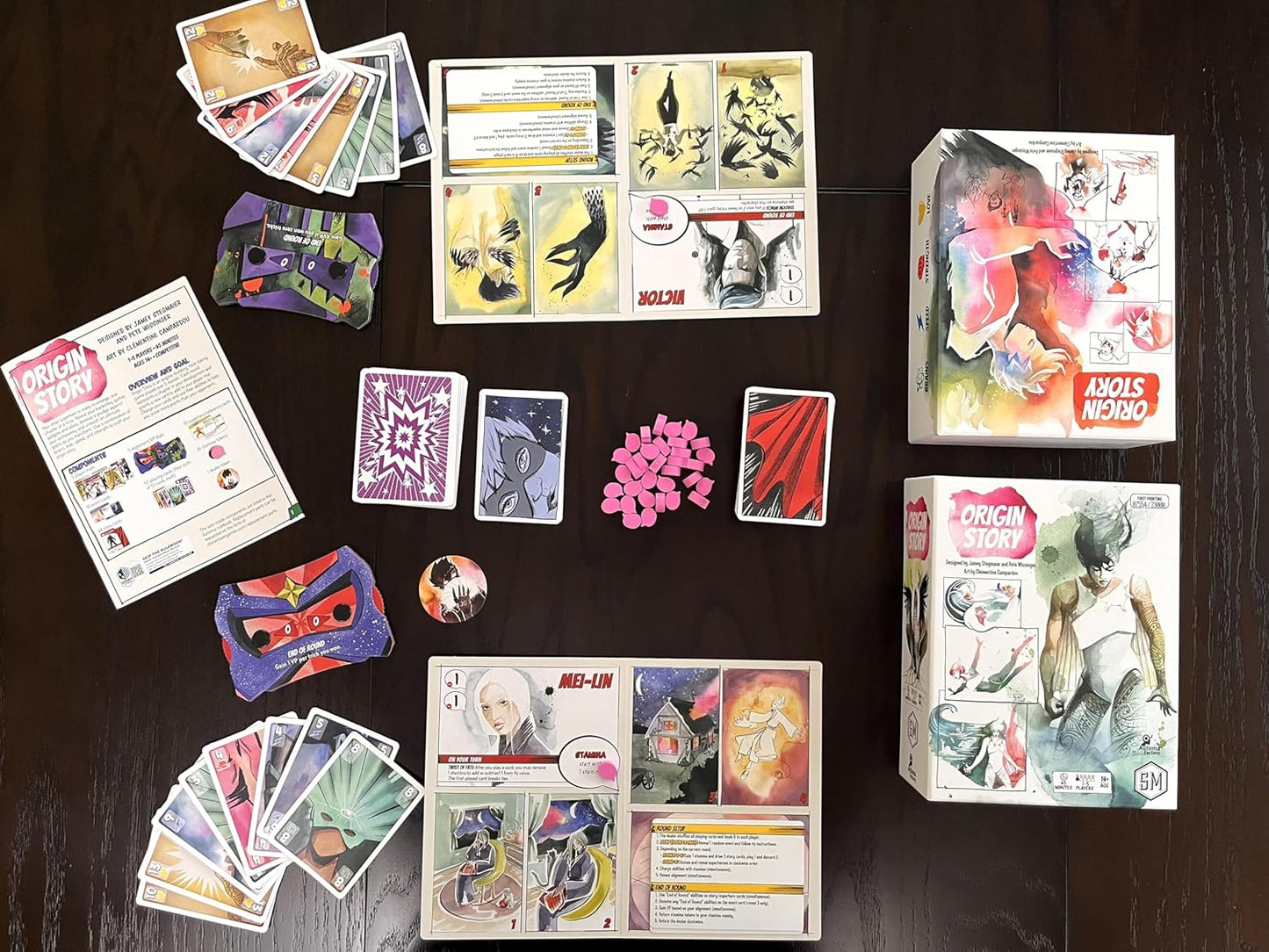 Collection of game pieces, cards and packaging for Origin Story card game, on a dark surface