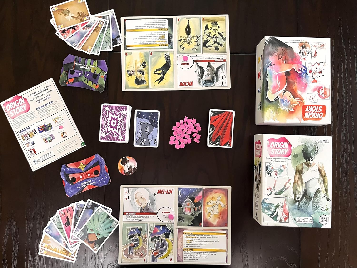 Collection of game pieces, cards and packaging for Origin Story card game, on a dark surface