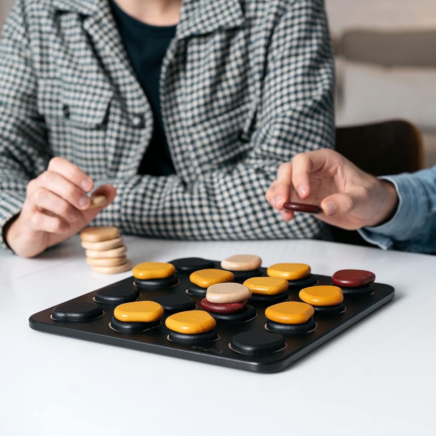 Two people playing Qawale game with colourful pieces on a board.