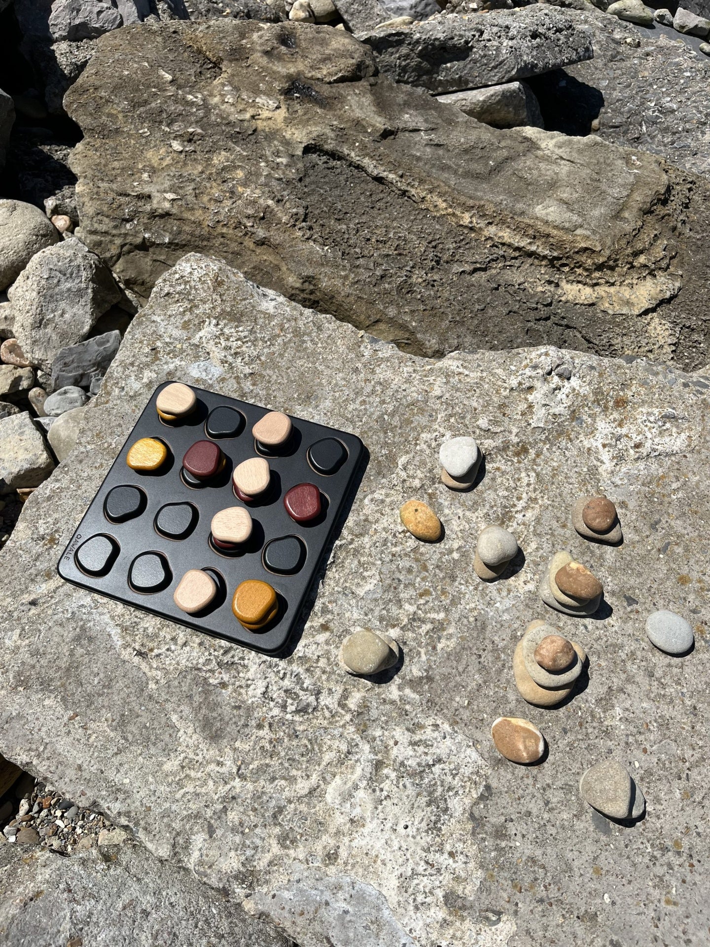 Qwale board game set on rocks with pebbles copying board game