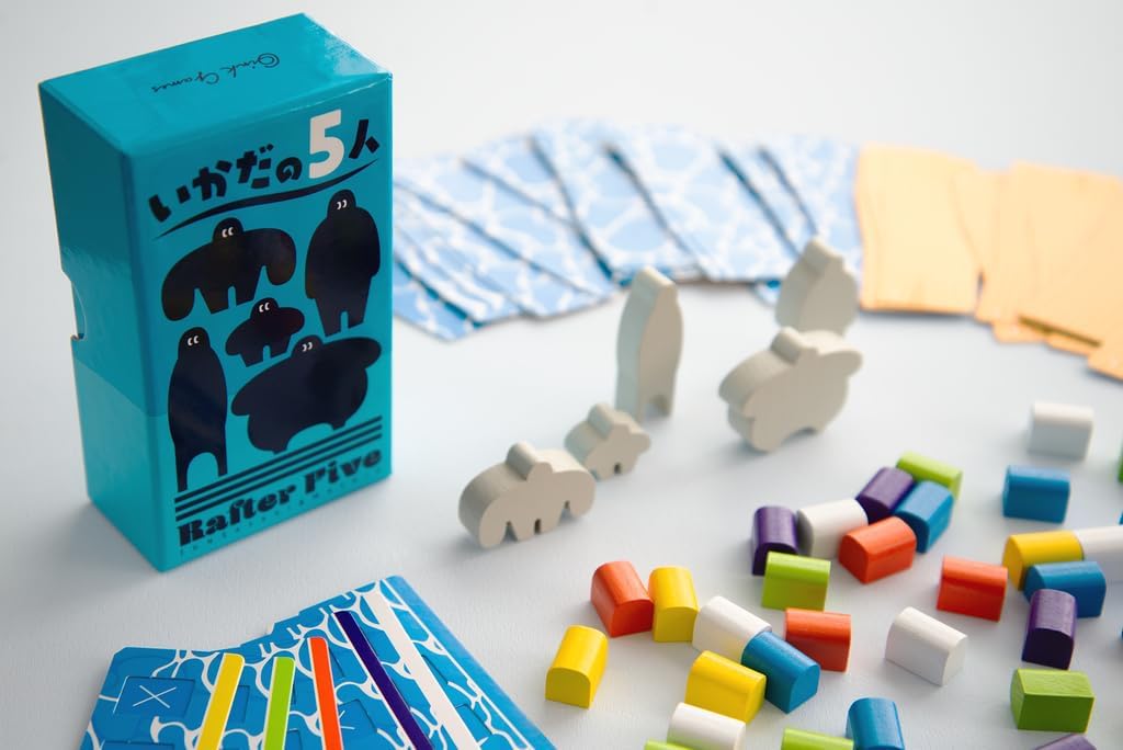Board game components including a blue box, colourful pieces, and animal-shaped tokens on a light surface.