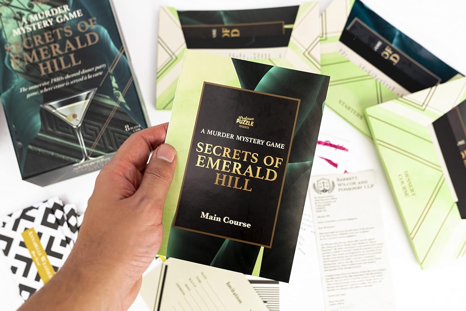 Hand holding a 'Secrets of Emerald Hill' murder mystery game book with packaging and other books in the background.
