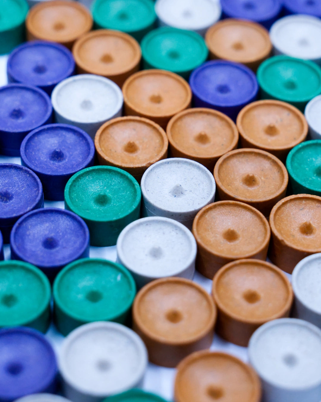 A close-up, top-down view of numerous small cylindrical plastic caps or lids in multiple colours for SETI: search for extraterrestrial intelligence board game, including blue, green, white, and tan, arranged closely together.