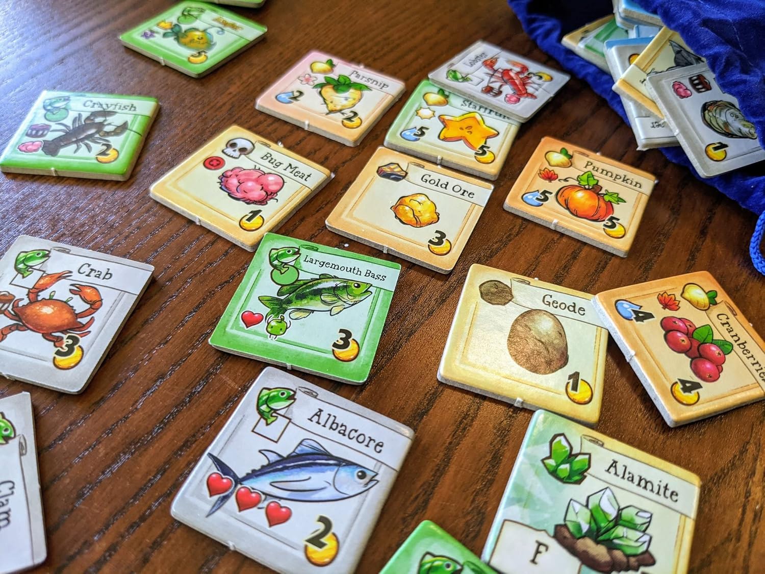 Collection of colourful game cards for Stardew Cooperative farming board game on a wooden surface