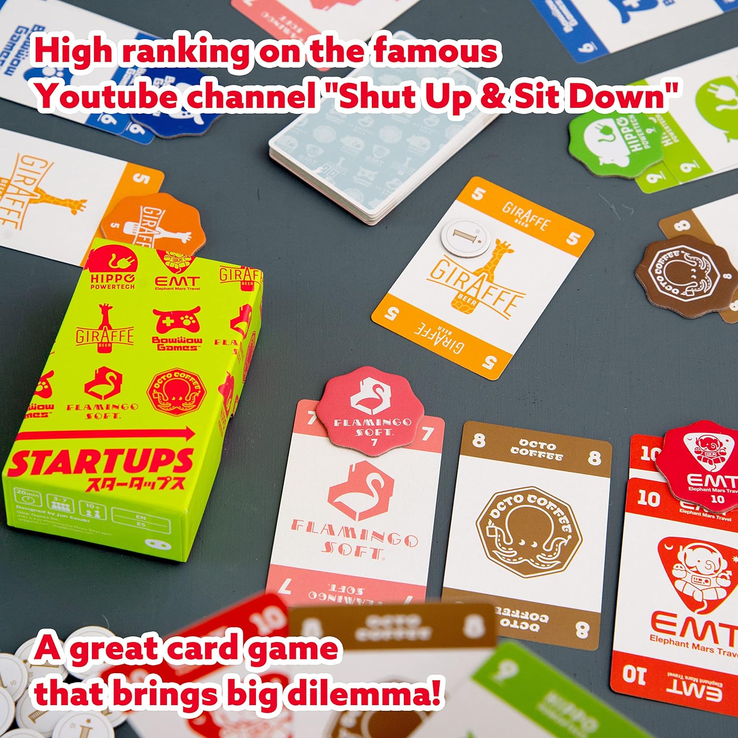 Startups card game with various cards and a box on a dark surface, featuring text about the game's ranking on a YouTube channel.