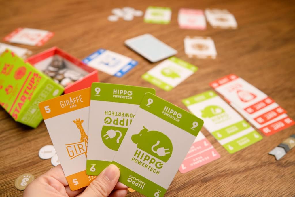Hand holding game cards with 'Hippo' branding on a wooden surface with scattered game pieces.