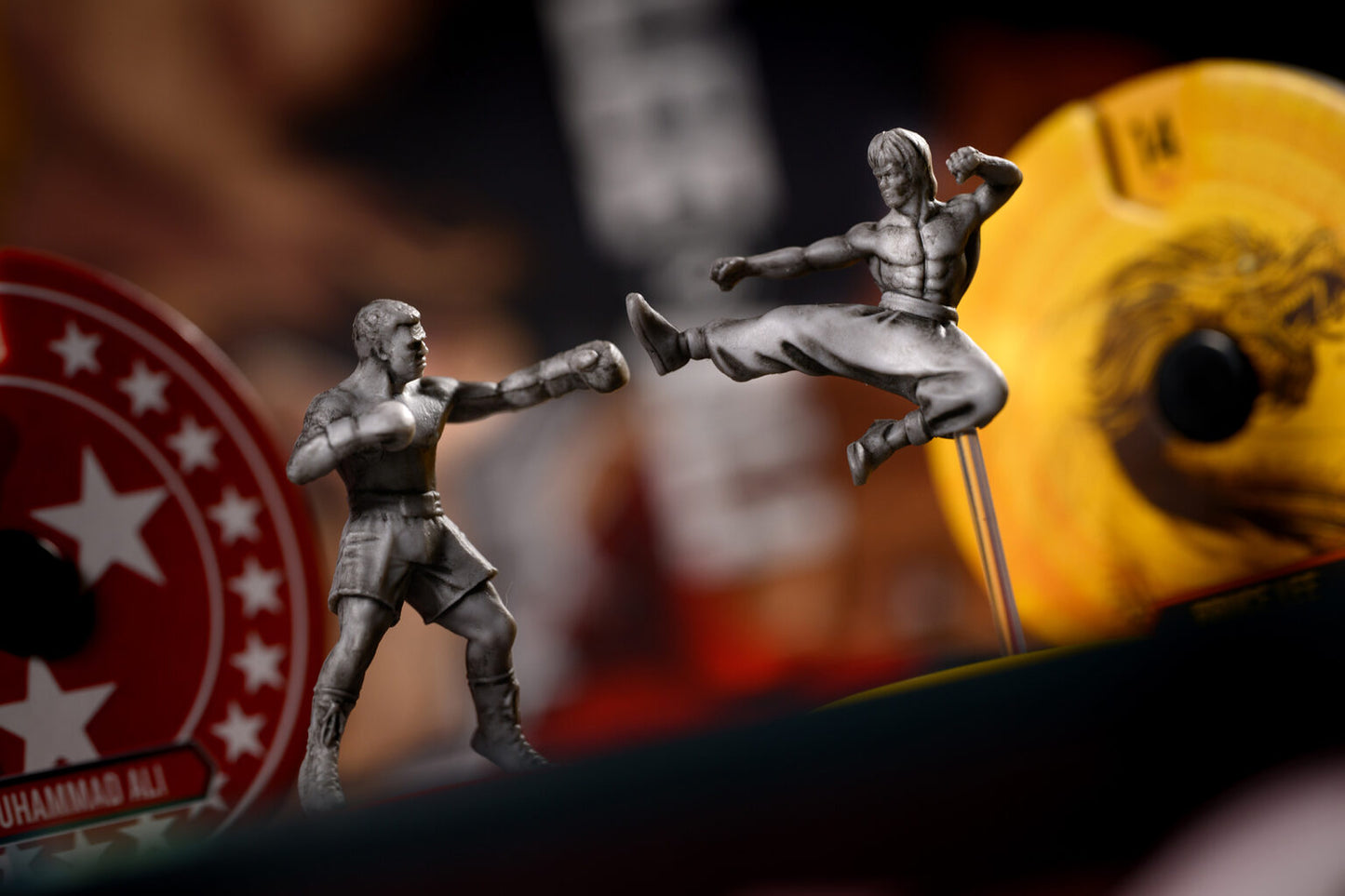 Two action figure toys in a dynamic pose with a blurred background featuring a logo for Unmatched lee vs ali board game