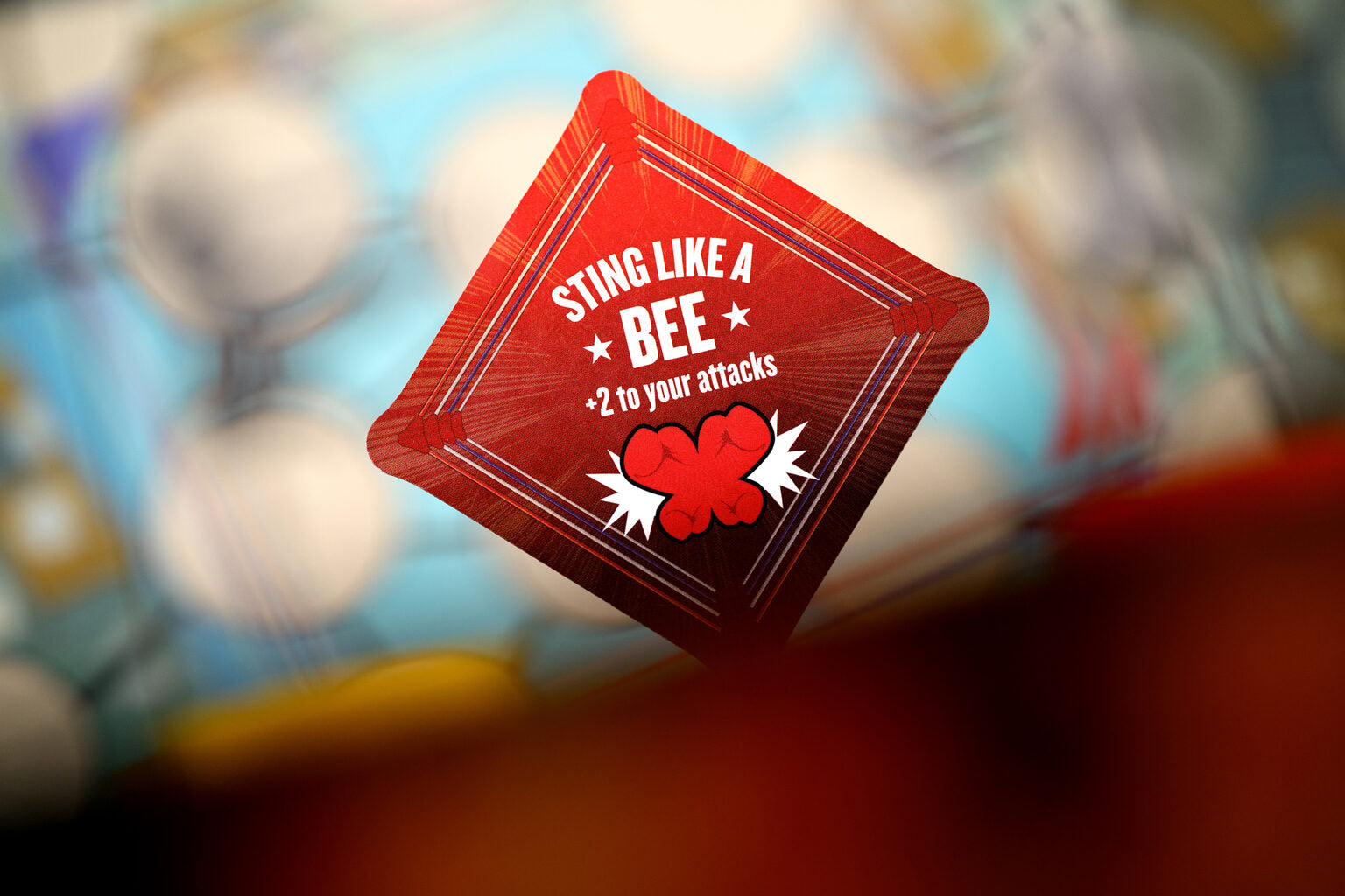 Red game token with sting like a bee +2 to your attacks text on a blurred background