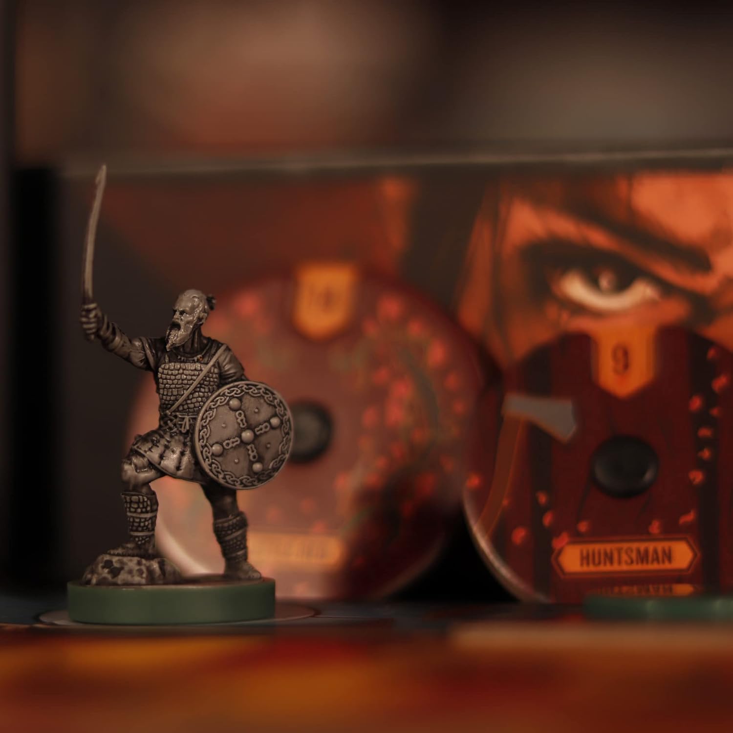 Miniature figurine of a warrior with a sword and shield, set against a blurred background with a mask.