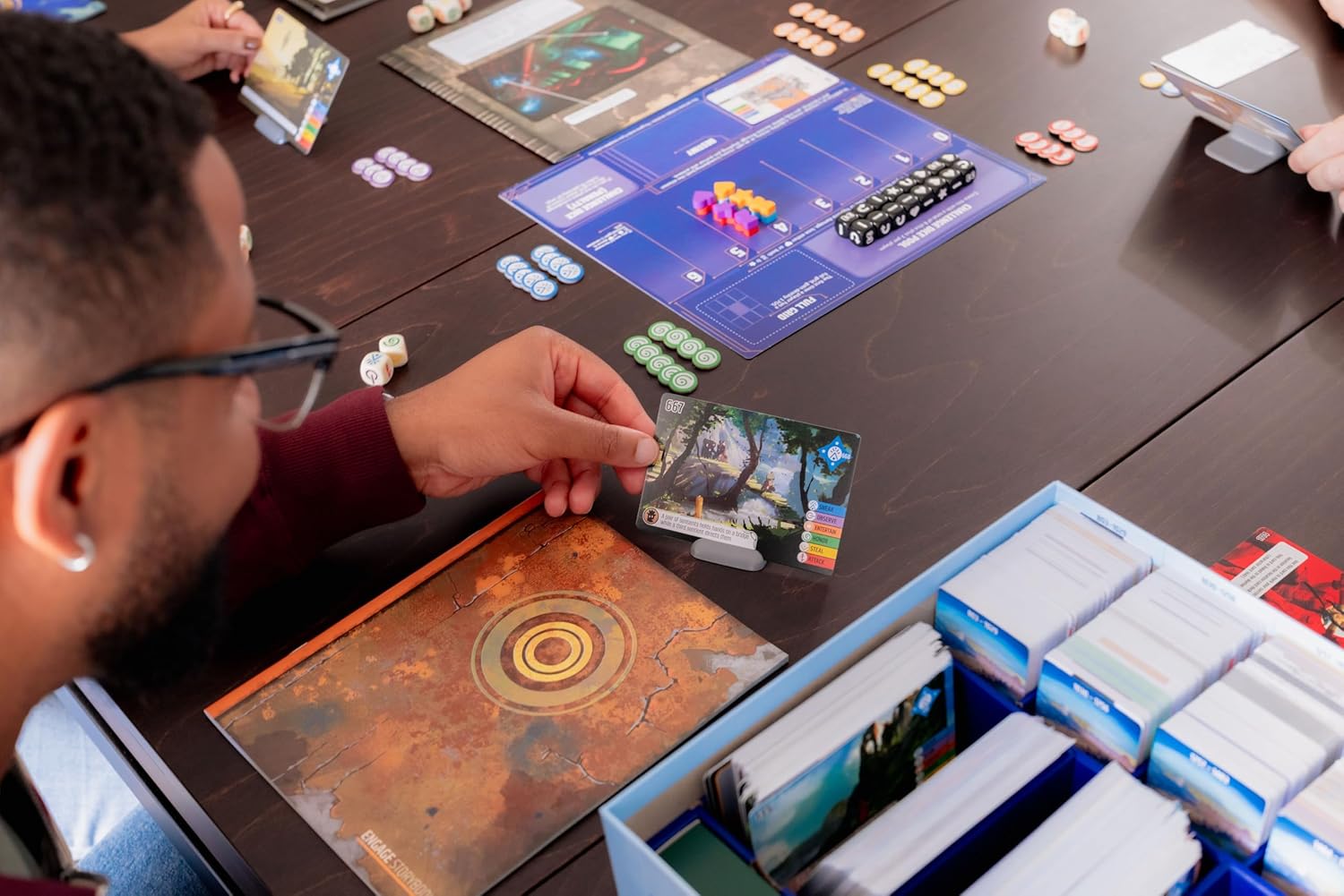 Person playing Vantage the board game with various game pieces and cards on a table.